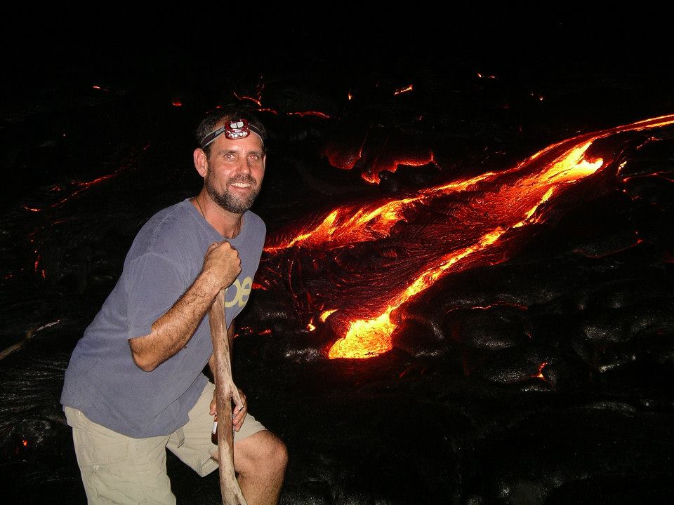 Scott, wearing a headlamp, crouched beside a glowing lava flow at night