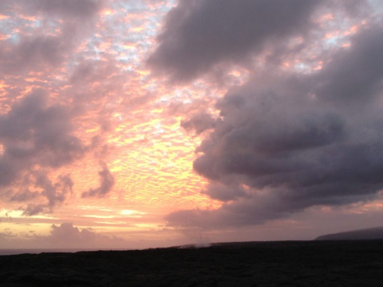 Pink and violet clouds over a dark lava field at sunset