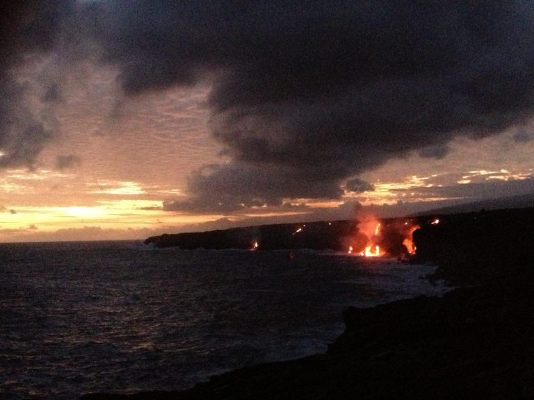 Lava entering the ocean at sunset beneath storm clouds
