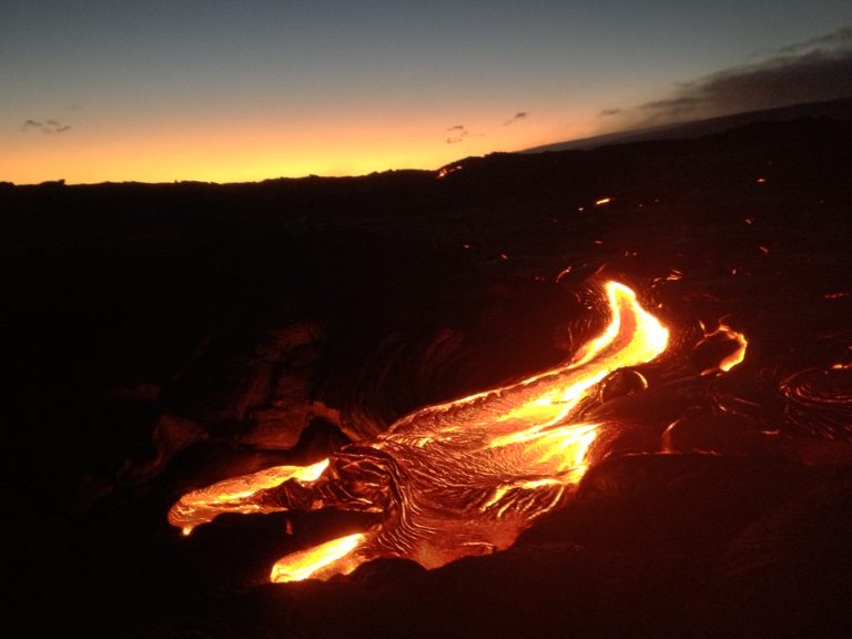 A glowing lava flow at twilight under a darkening sky