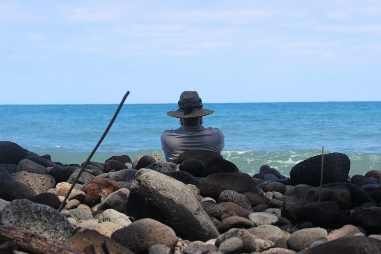 A hiker resting on smooth boulders beside the ocean