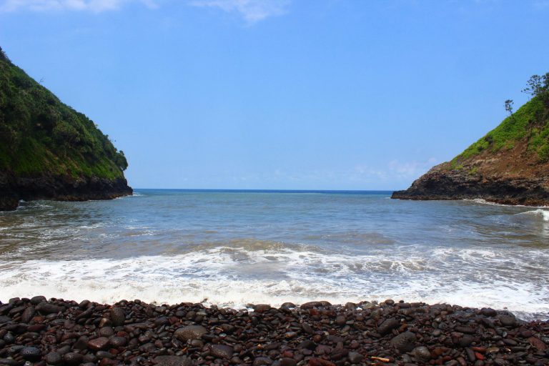 A small cove between green cliffs with surf rolling in