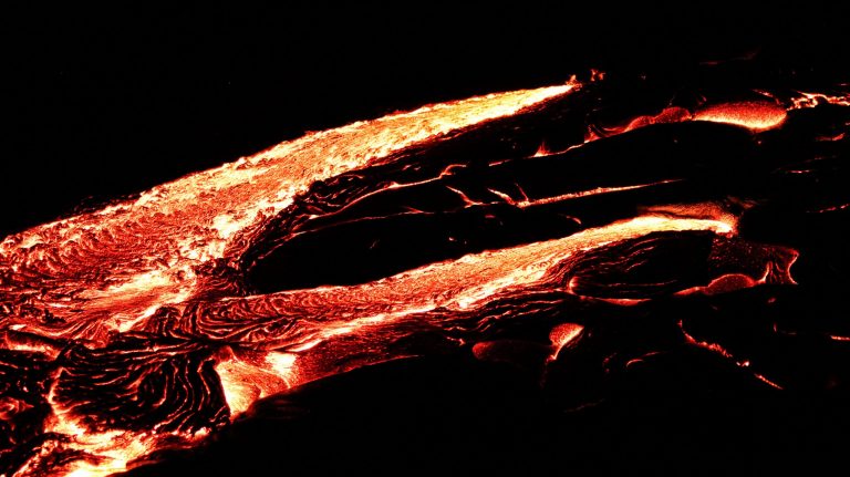 Streams of glowing lava against black rock at night