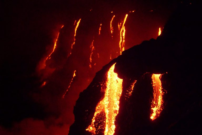 Streams of lava pouring down a dark slope at night