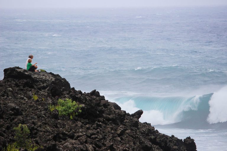 A person sitting on a lava cliff above crashing waves